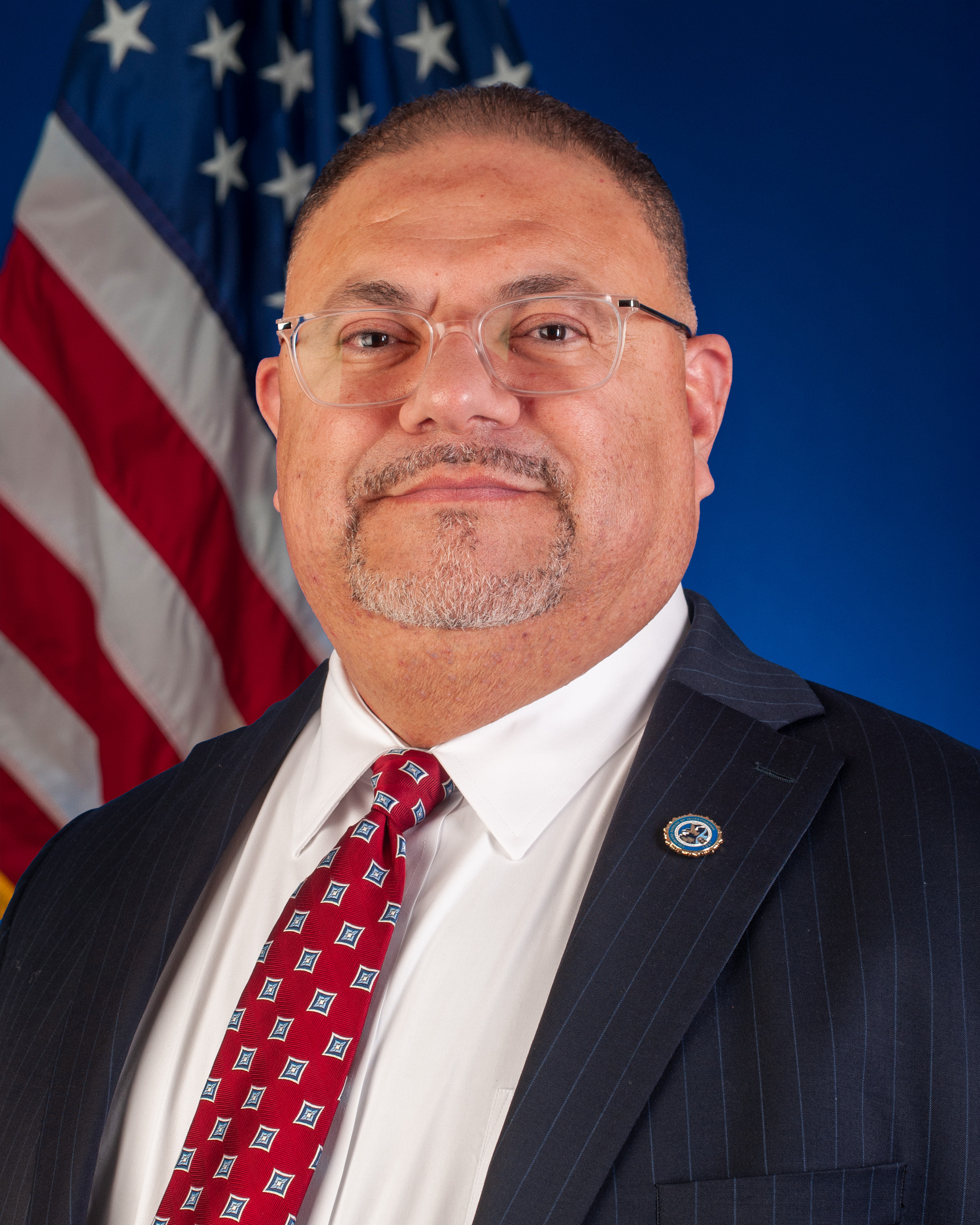 Photo of Armando Saldate III wearing a suite in front of the American flag