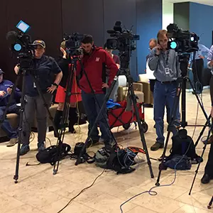 Three cameramen stand behind television cameras pointed in the same direction.