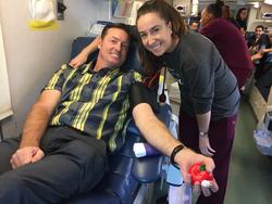 John Emsen sits in a reclining chair squeezing a ball to give blood while his daughter smiles on.