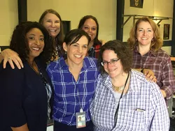 six women in plaid shirts smile for the camera