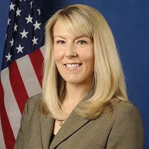 photo of Jana locke in a brown suit with an american flag behind her