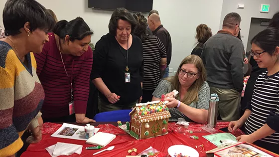 A diverse group of women help each other build a gingerbread house