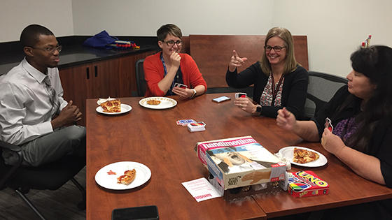 A man and three women eat pizza and play a card game