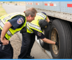 two port of entry workers in yellow reflective vests examine a semi truck tire