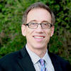 photo of Joe Thome wearing a dark suit jacket, light shirt and glasses